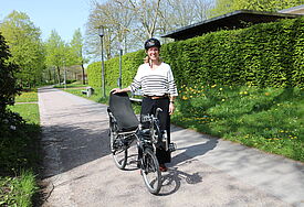 Die Bischöfin trägt einen Fahrradhelm und steht draußen im Grünen neben ihrem Liegerad.