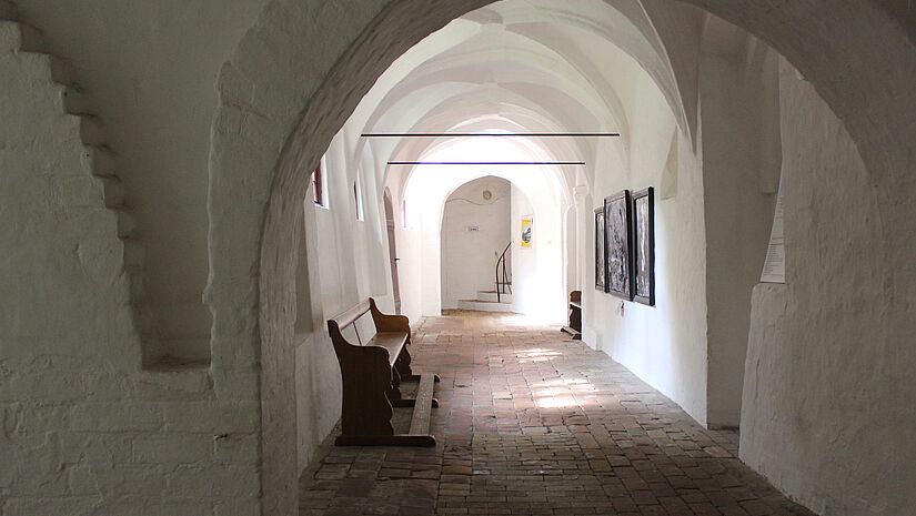 Blick in einen mittelalterlichen, weiß gestrichenen Kreuzgang mit Rundbögen und Kreuzgewölben. 