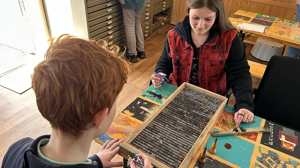Karl und Sina setzen in der Museumswerkstatt die Buchstaben für einen kleinen Postkarten-Gruß. 