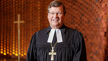 Bischof Abromeit im Talar mit Bischofskreuz an einer Kette in einer Kirche